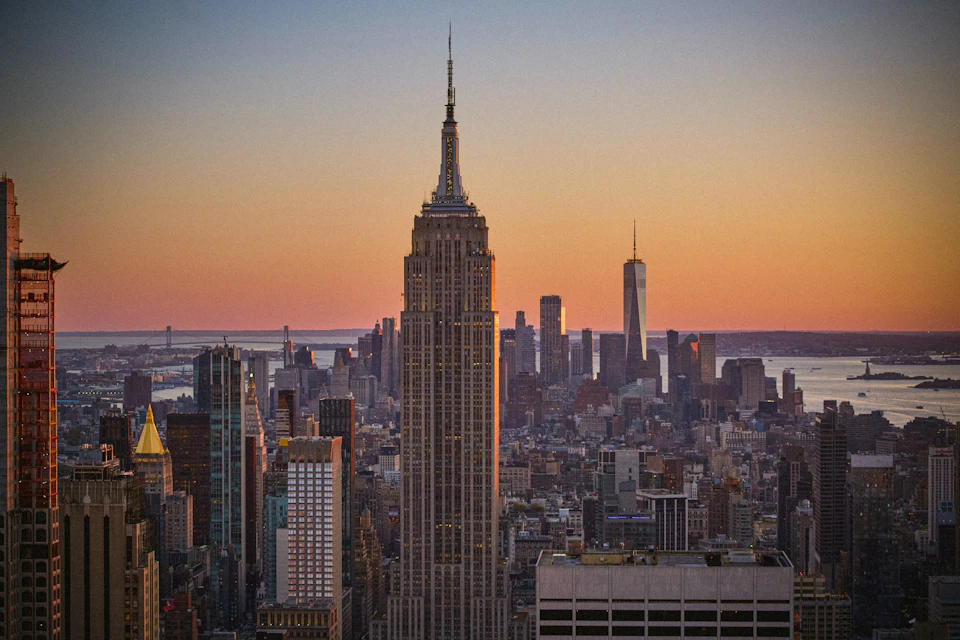 Sunset view of a cityscape featuring the Empire State Building in the foreground and One World Trade Center in the background.