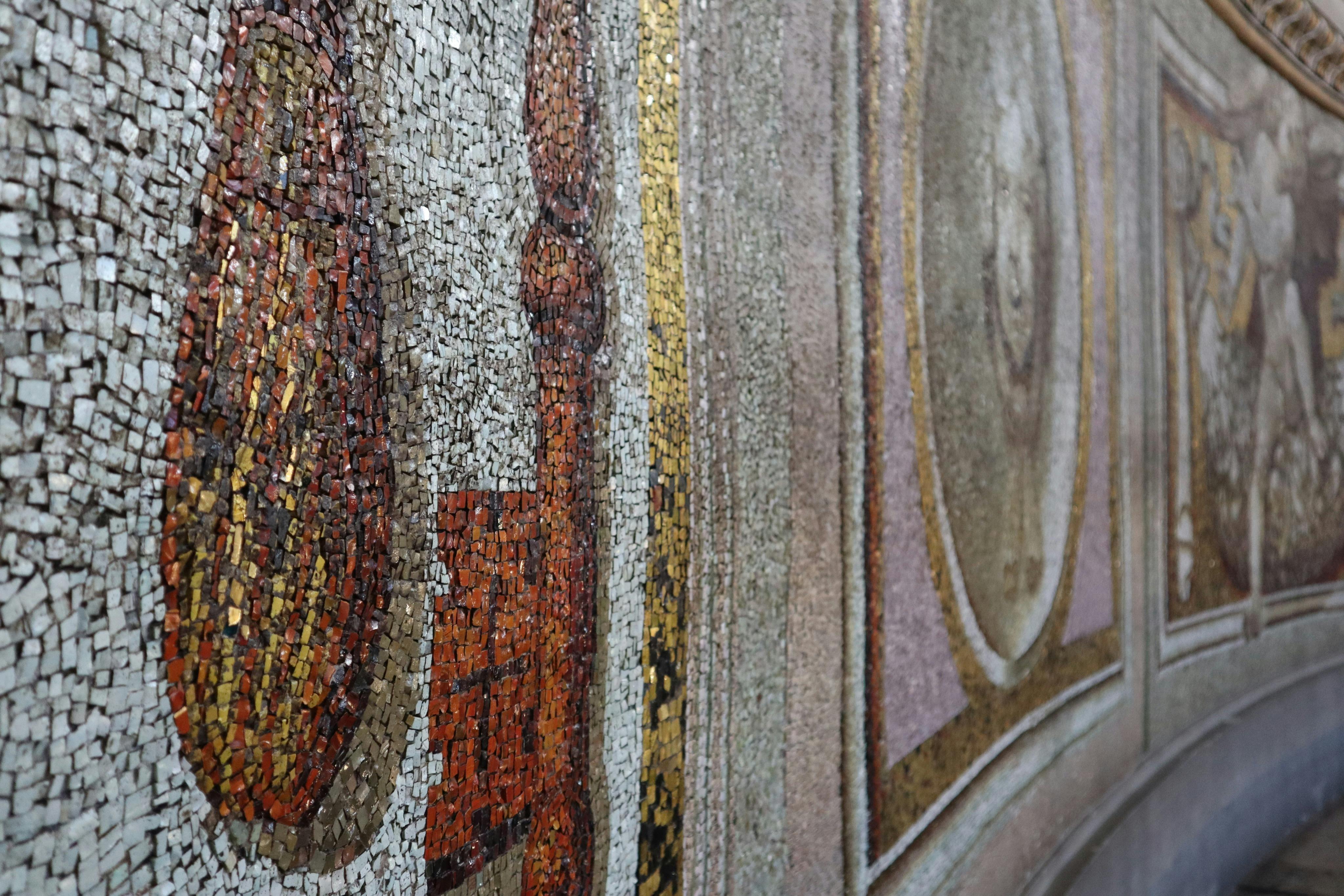 Primo piano di una dettagliata parete a mosaico con motivi intricati e una combinazione di toni della terra e accenti dorati.