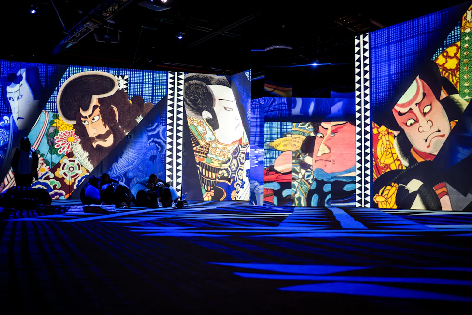 A vibrant indoor digital art installation featuring traditional Japanese kabuki-style portraits on illuminated walls.
