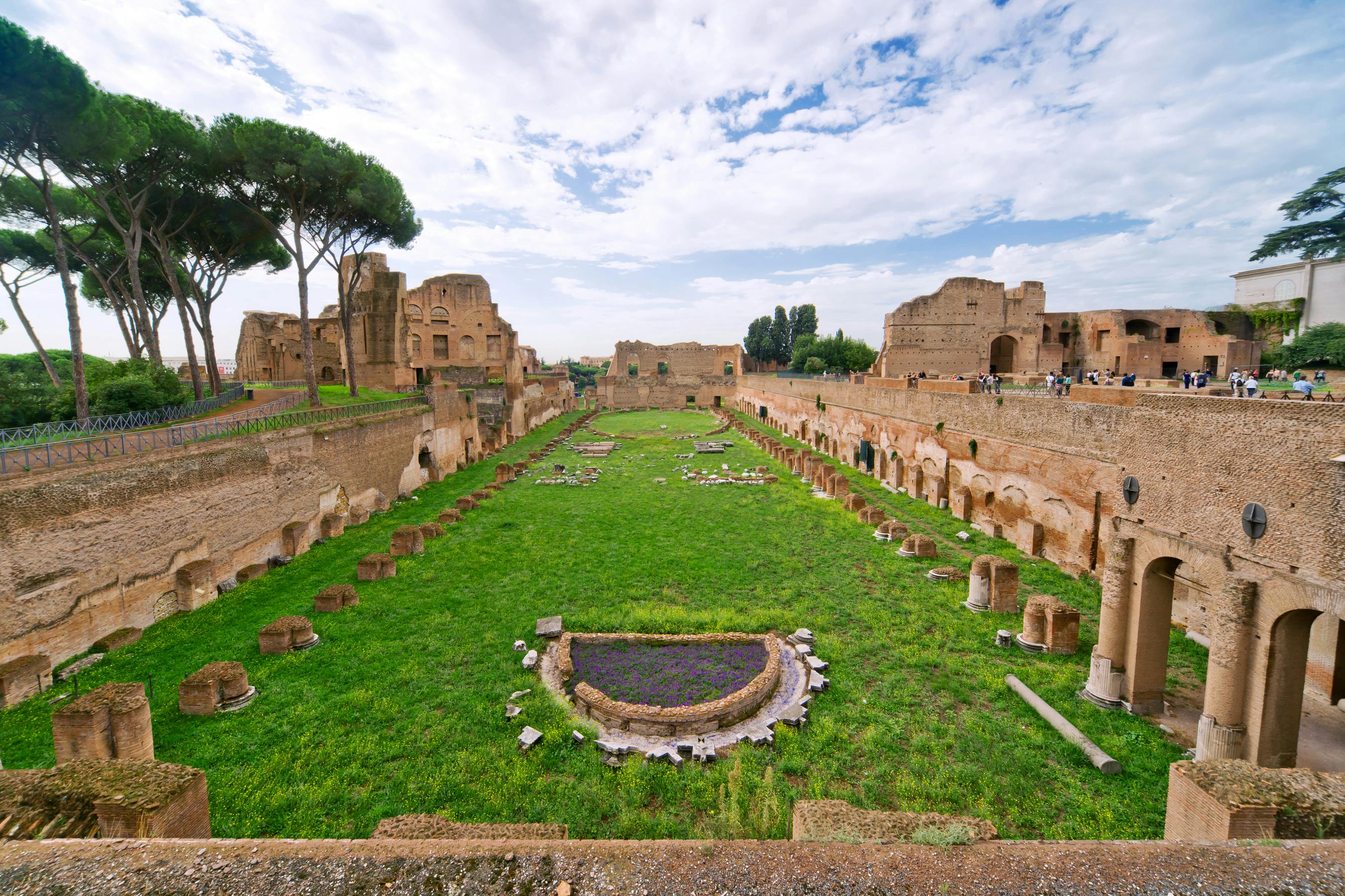 An ancient Roman ruins site with grass, stone columns, and remnants of structures under a partly cloudy sky.