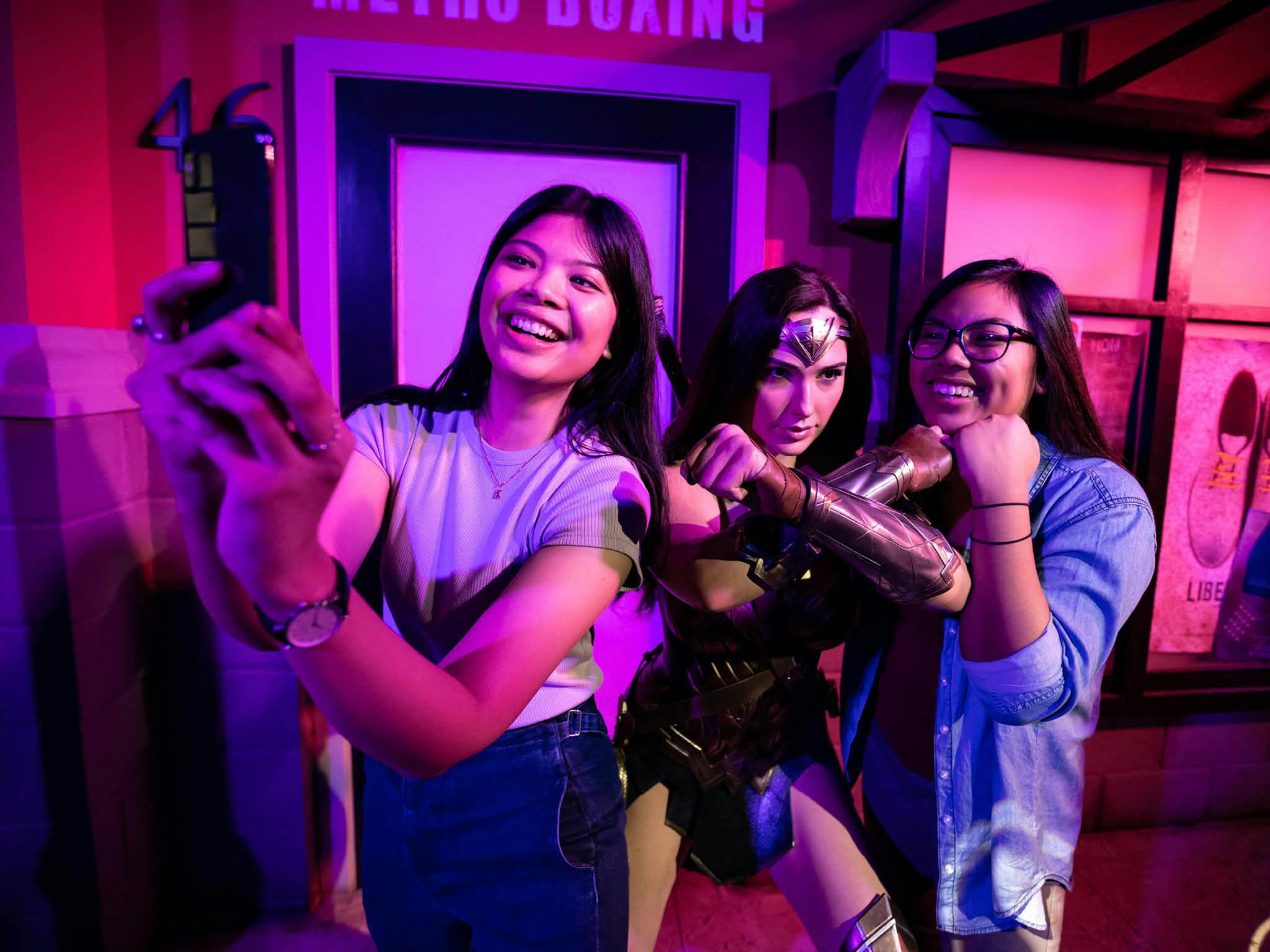 在灯光充满活力的房间里，两位微笑的女士在神奇女侠雕像旁摆姿势。