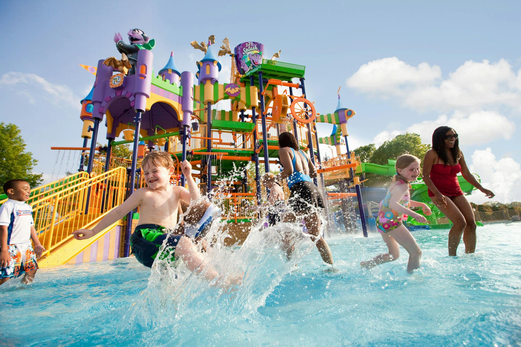 Kinderen spelen en spetteren in een waterpark met kleurrijke structuren en glijbanen op de achtergrond.