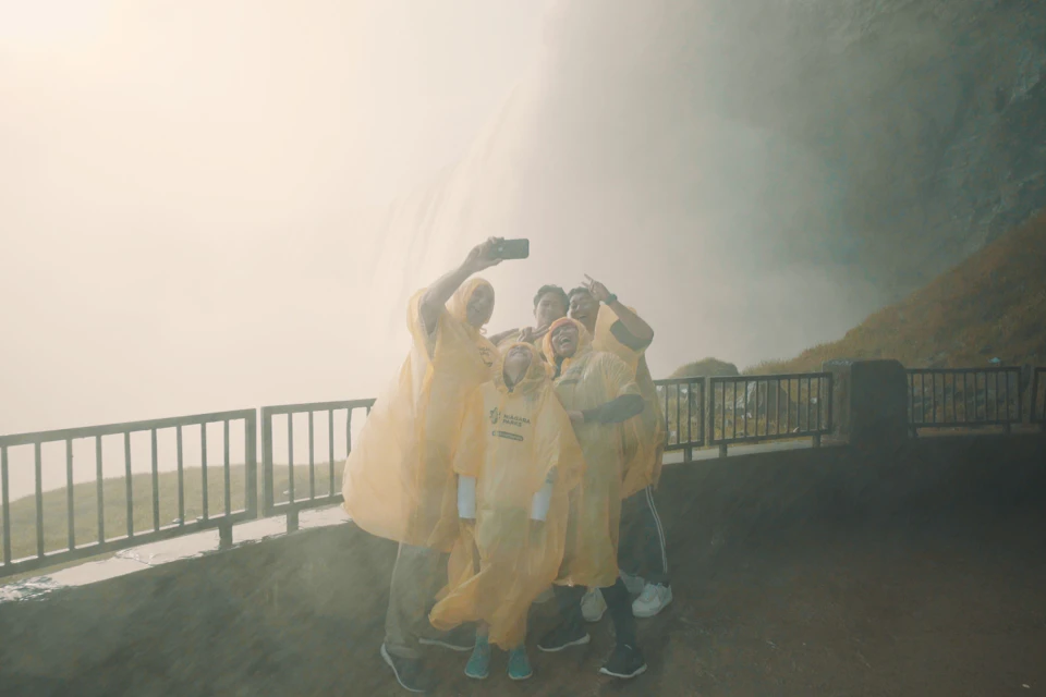 A group on a viewing platform at the Journey Behind the Falls Experience, posing for a photo with Horseshoe Falls behind them
