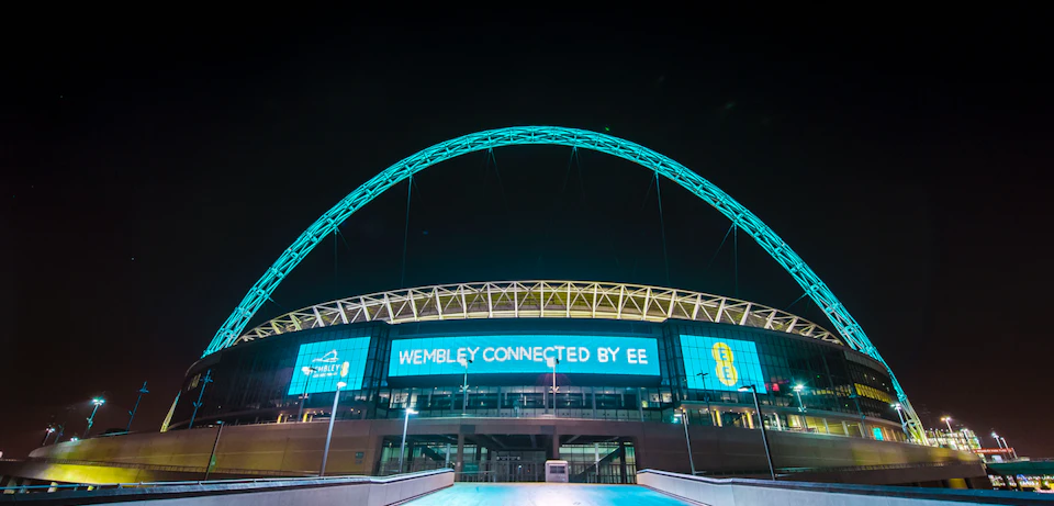 Night view of Wembley Stadium with its lit-up arch and screens displaying "Wembley Connected by EE."