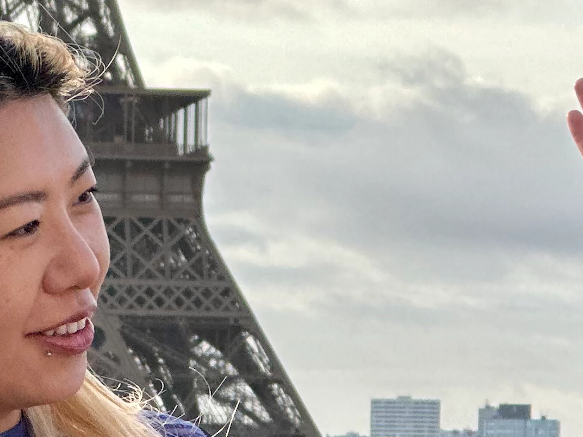 Three people smiling and talking near the Eiffel Tower with a cloudy sky in the background.