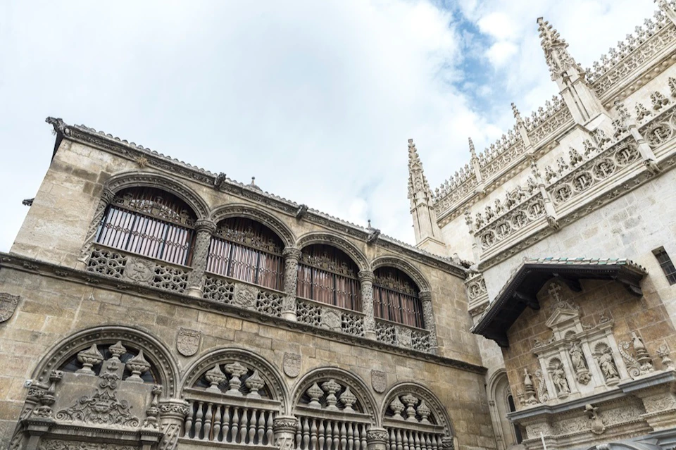 Ornate historic building with arched windows, intricate stone carvings, and spires against a partly cloudy sky.