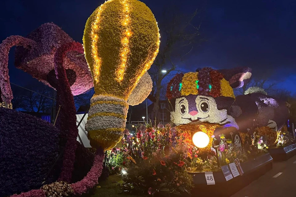 A nighttime floral display featuring a hot air balloon and a colorful animal figure, illuminated with lights.