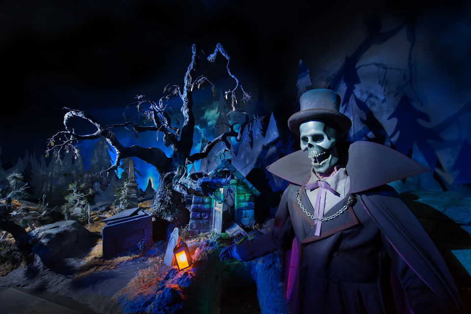 A skeleton dressed in a formal suit and top hat in a spooky, dimly lit scene with a twisted tree and tombstones.