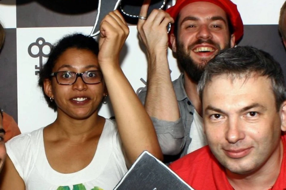 A group of six people posing with blackboard-style speech bubble props with various messages written on them.