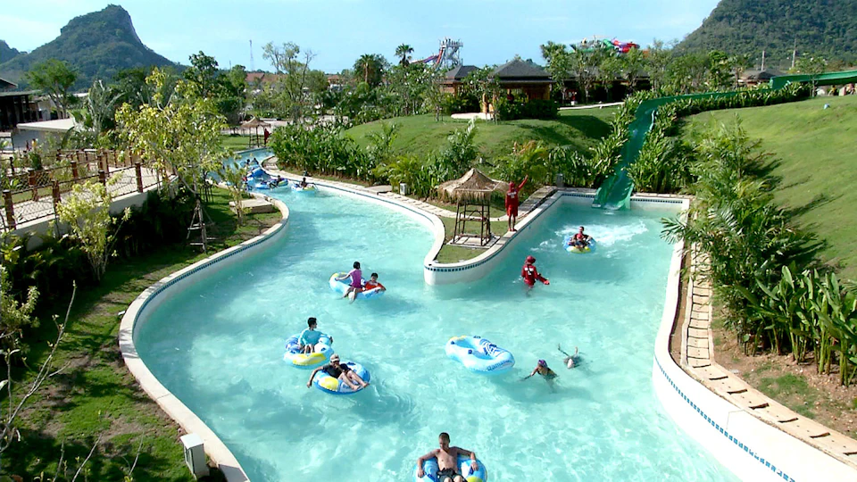 People floating on inflatable tubes in a lazy river at a water park, surrounded by greenery and structures.