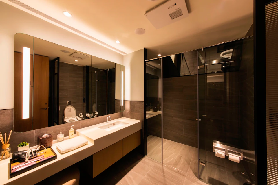 Modern bathroom with a sink, mirror, glass-enclosed shower, toilet, and warm lighting.