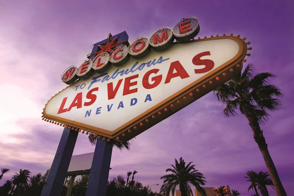 Illuminated "Welcome to Fabulous Las Vegas, Nevada" sign with palm trees in the background under a purple sky.
