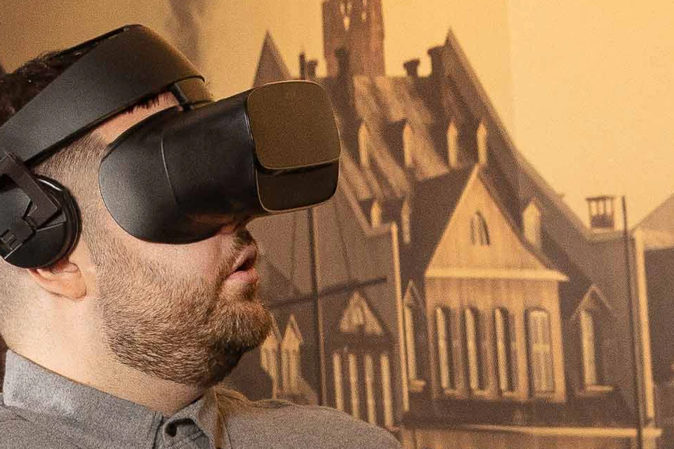 Two people wearing VR headsets sit in a ride with ornate rails, smiling and reaching out as if interacting with a virtual environment.
