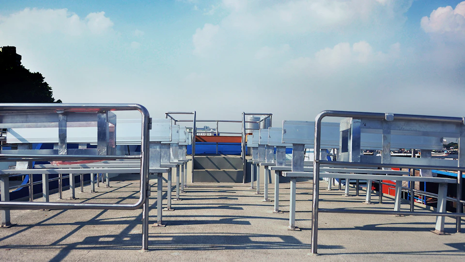 Empty outdoor patio seating with rows of metal benches and tables, under a clear blue sky.