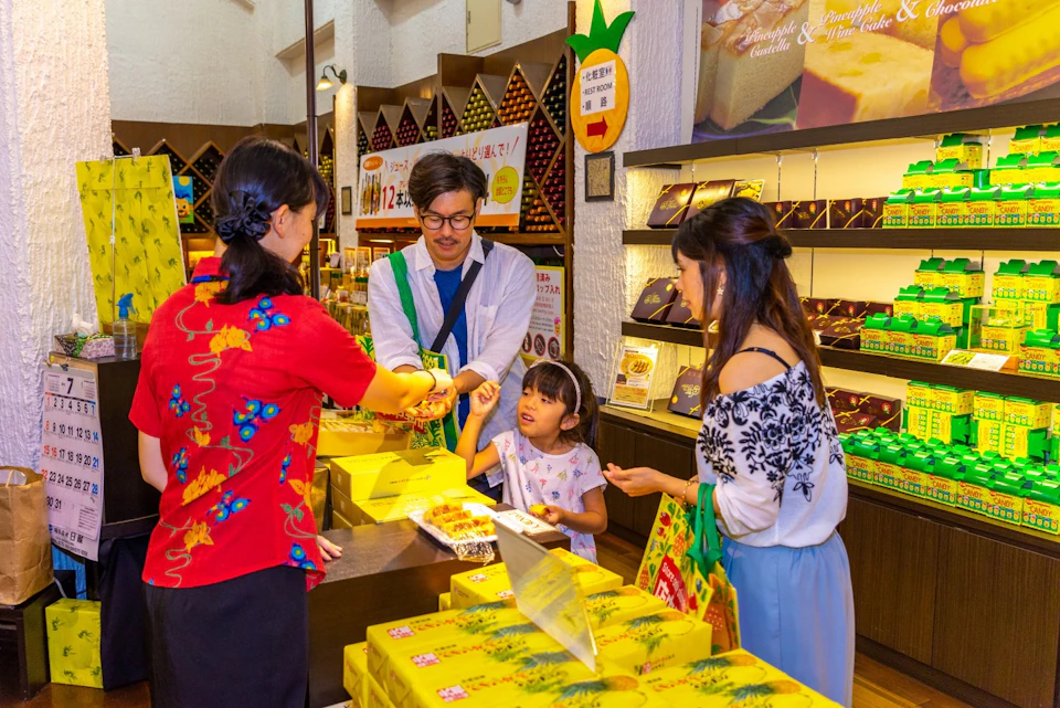 A shop employee in a red shirt assists a family with a young child in a store with yellow-packaged products on display.
