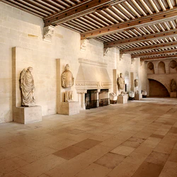 En stor hall med höga takbjälkar, stenstatyer längs väggarna och en stor öppen spis.