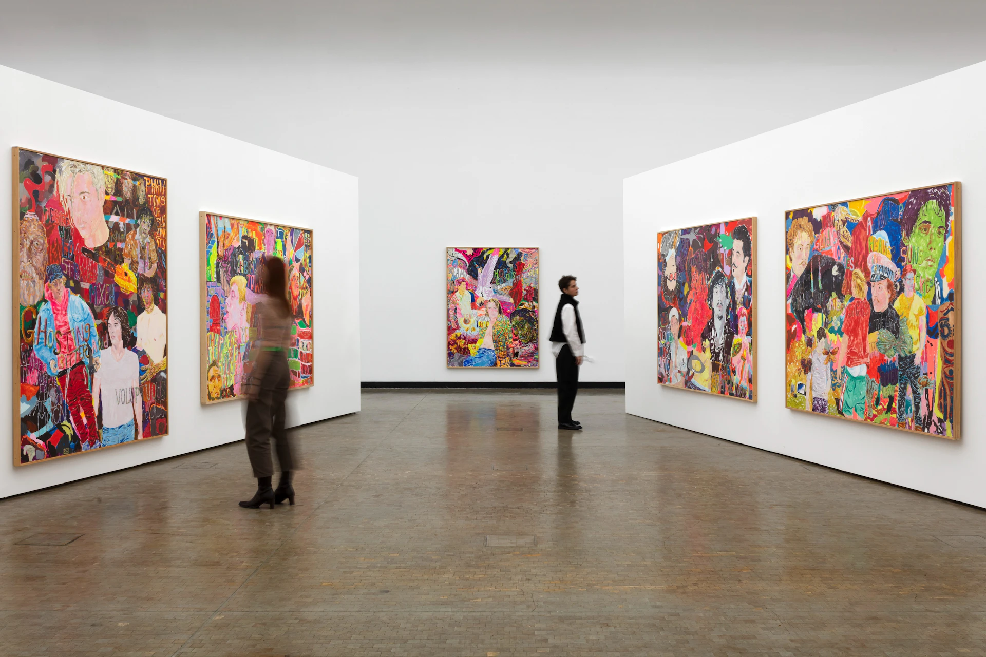 A gallery space with colorful paintings displayed on white walls and two people observing the art.