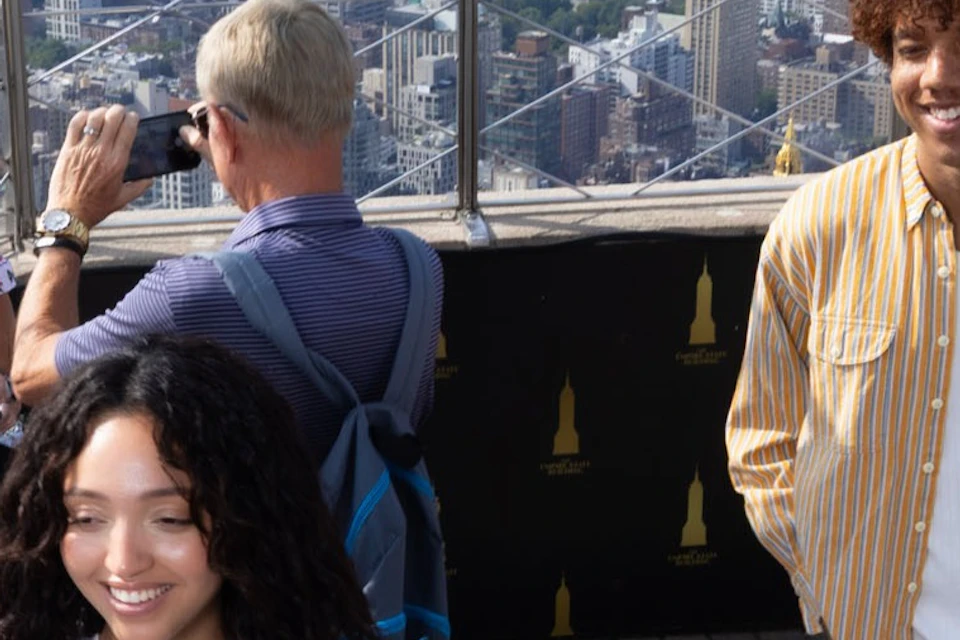 A group of people standing and walking on an observation deck with a city skyline visible in the background.