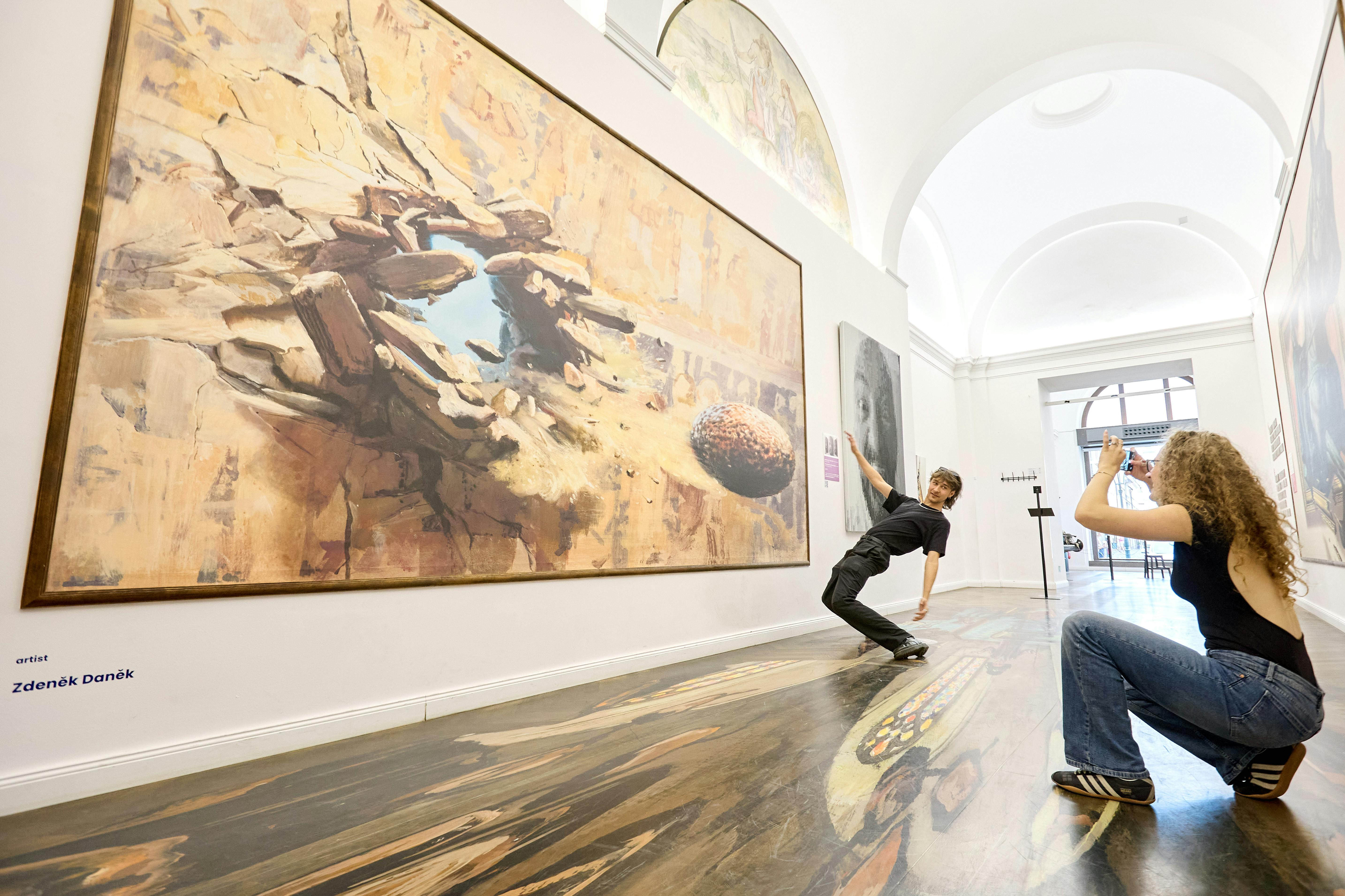 En person læner sig dramatisk op ad et gulv, der er malet for at fremstå tredimensionelt i et kunstgalleri, og interagerer med kunstværket.