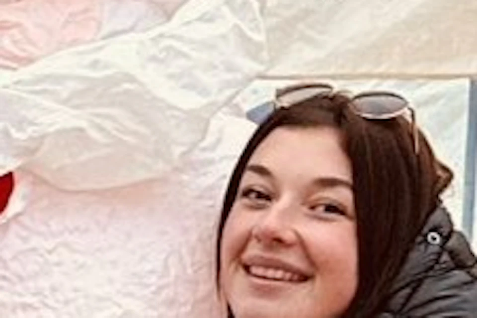 Two people pose with a large inflatable Santa Claus outside, with two other people inside a tent in the background.
