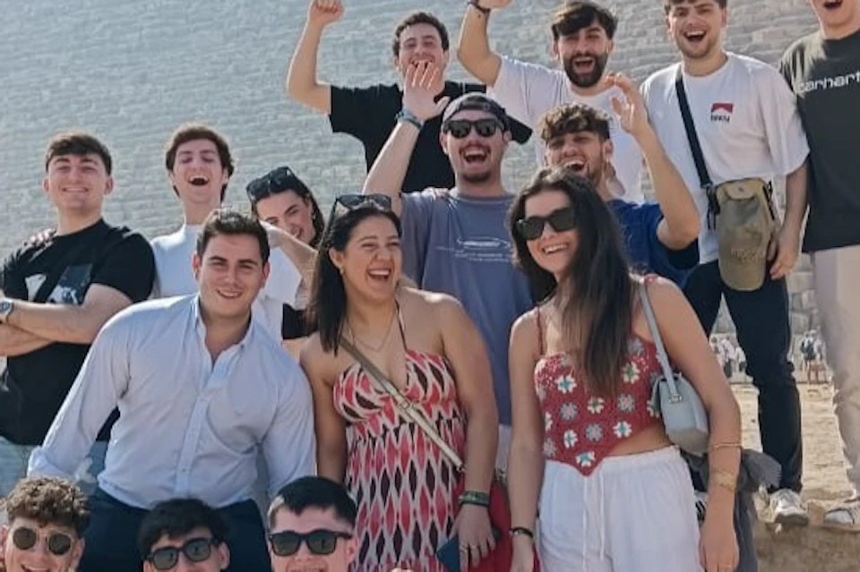 A group of people smiling and posing in front of a pyramid under a clear blue sky.