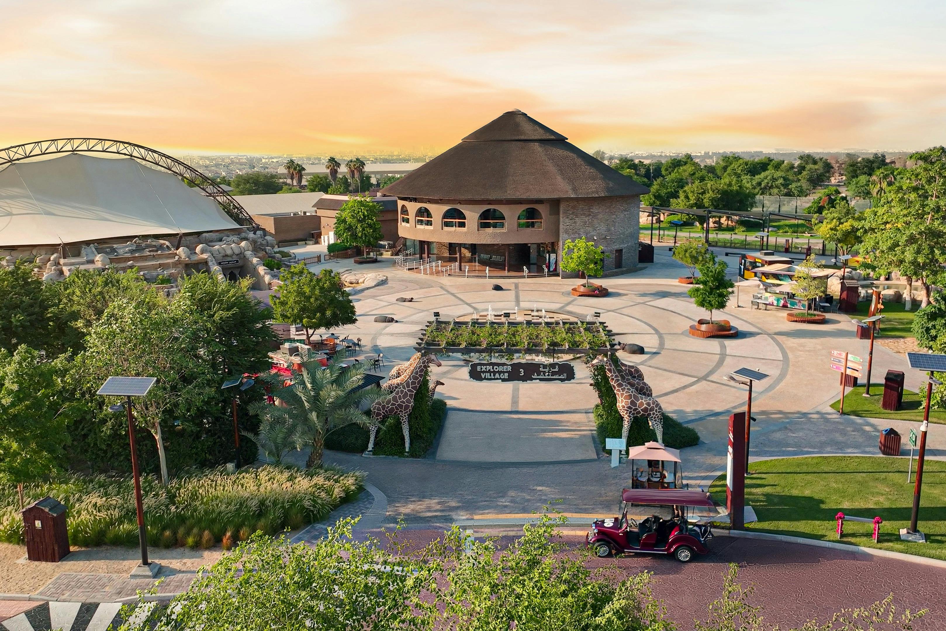 Κυκλική πλατεία με ένα κεντρικό κτίριο, επενδεδυμένο με δέντρα. Ένα κόκκινο βίντατζ αυτοκίνητο και αγάλματα καμηλοπάρδαλης τονίζουν την είσοδο.