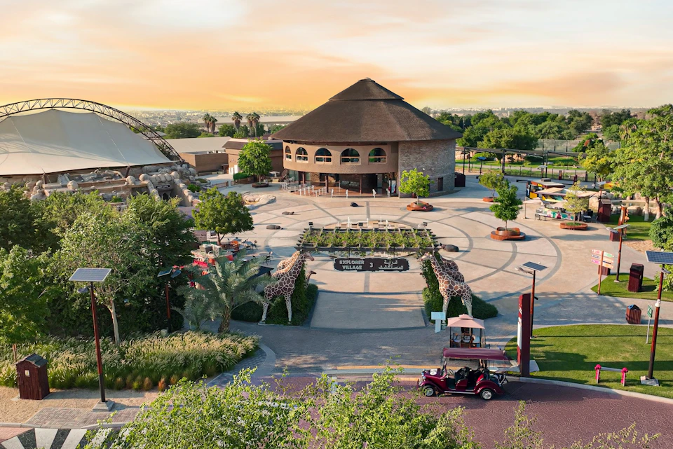 Circular plaza with a central building, lined with trees. A red vintage car and giraffe statues highlight the entrance.