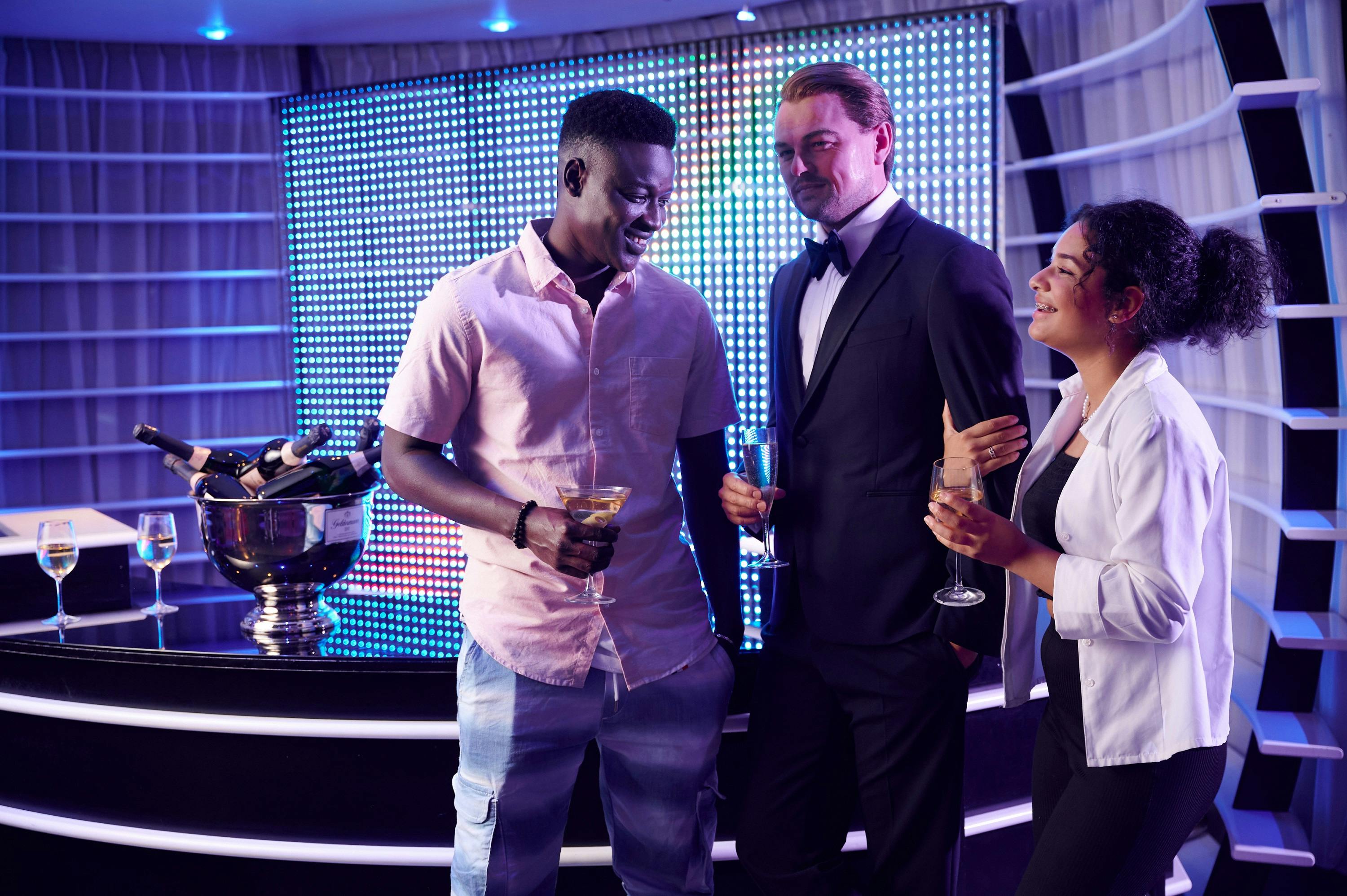 三个人穿着半正式的服装，微笑着拿着饮料，站在明亮的房间里，桌子旁边放着香槟桶。