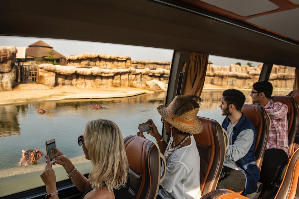 Three people sitting on a bus, looking out at a body of water and rocky landscape.