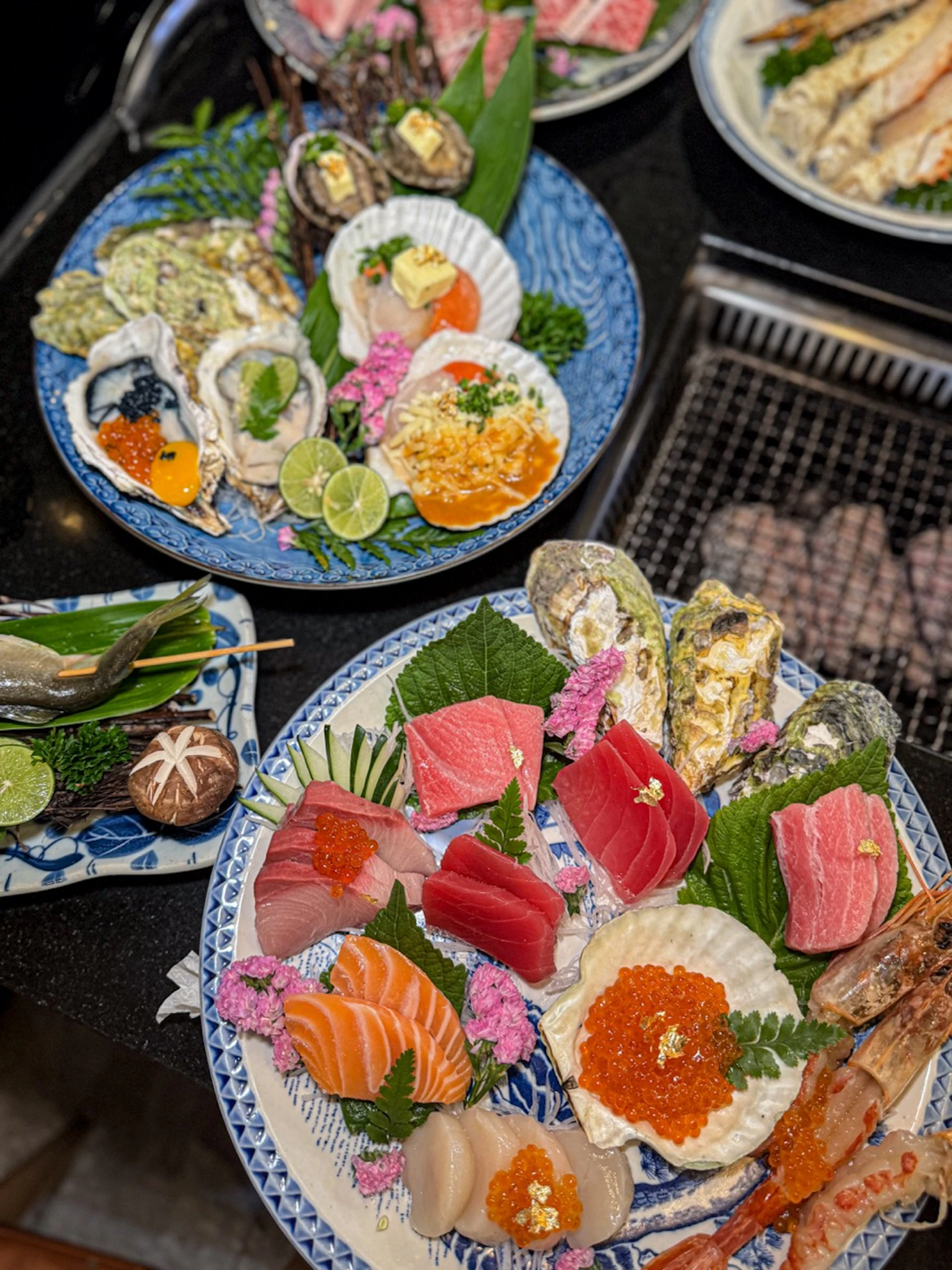 Plates of sashimi, oysters, and garnishes are artfully arranged on ceramic dishes, showcasing a variety of seafood delicacies.