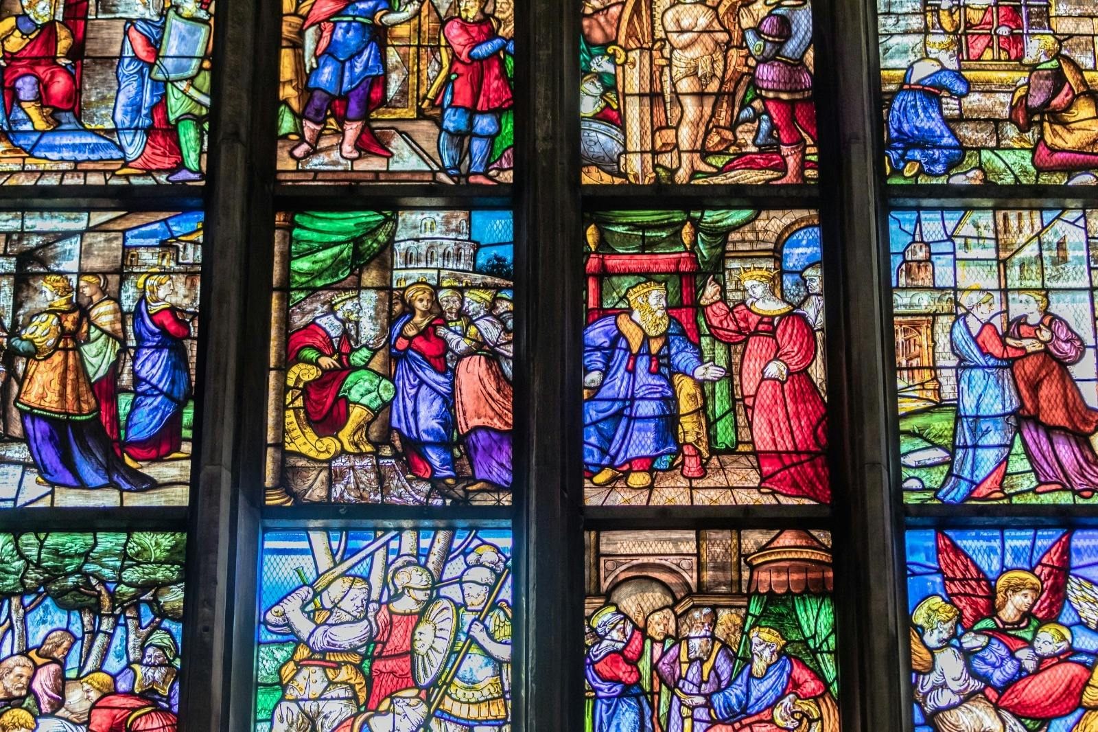 A stained glass window depicting various vibrant biblical scenes with people in historical attire and intricate details.