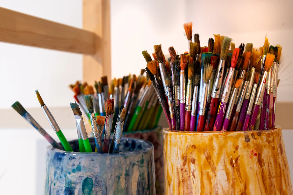 Three containers filled with various paintbrushes of different sizes and colours.