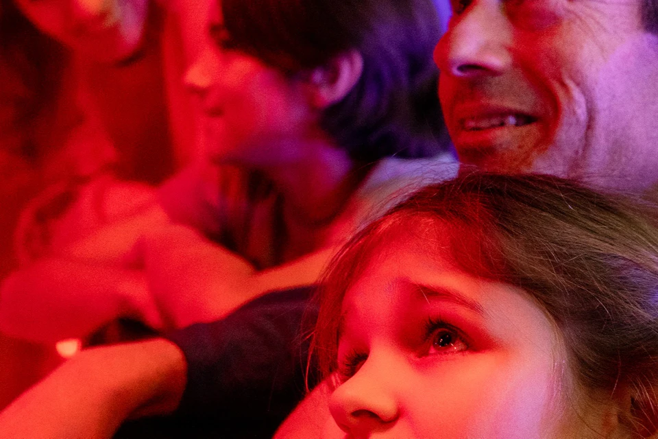 A group of four people leaning on a railing in a room with vibrant red and purple lighting, looking in various directions.