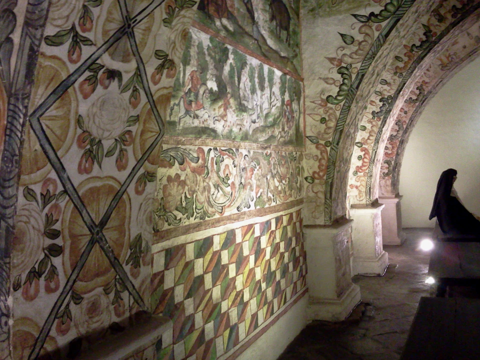 Interior of a historical building with walls decorated in intricate, brightly colored frescos and patterns, including floral and geometric designs.