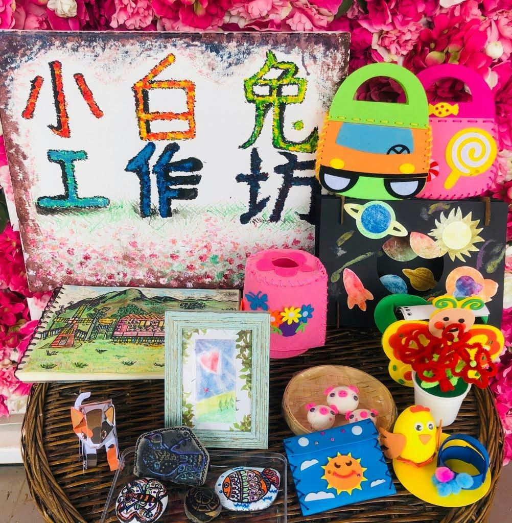 A colorful display of handmade crafts, including painted bags, framed art, clay figures, and decorative items on a table.