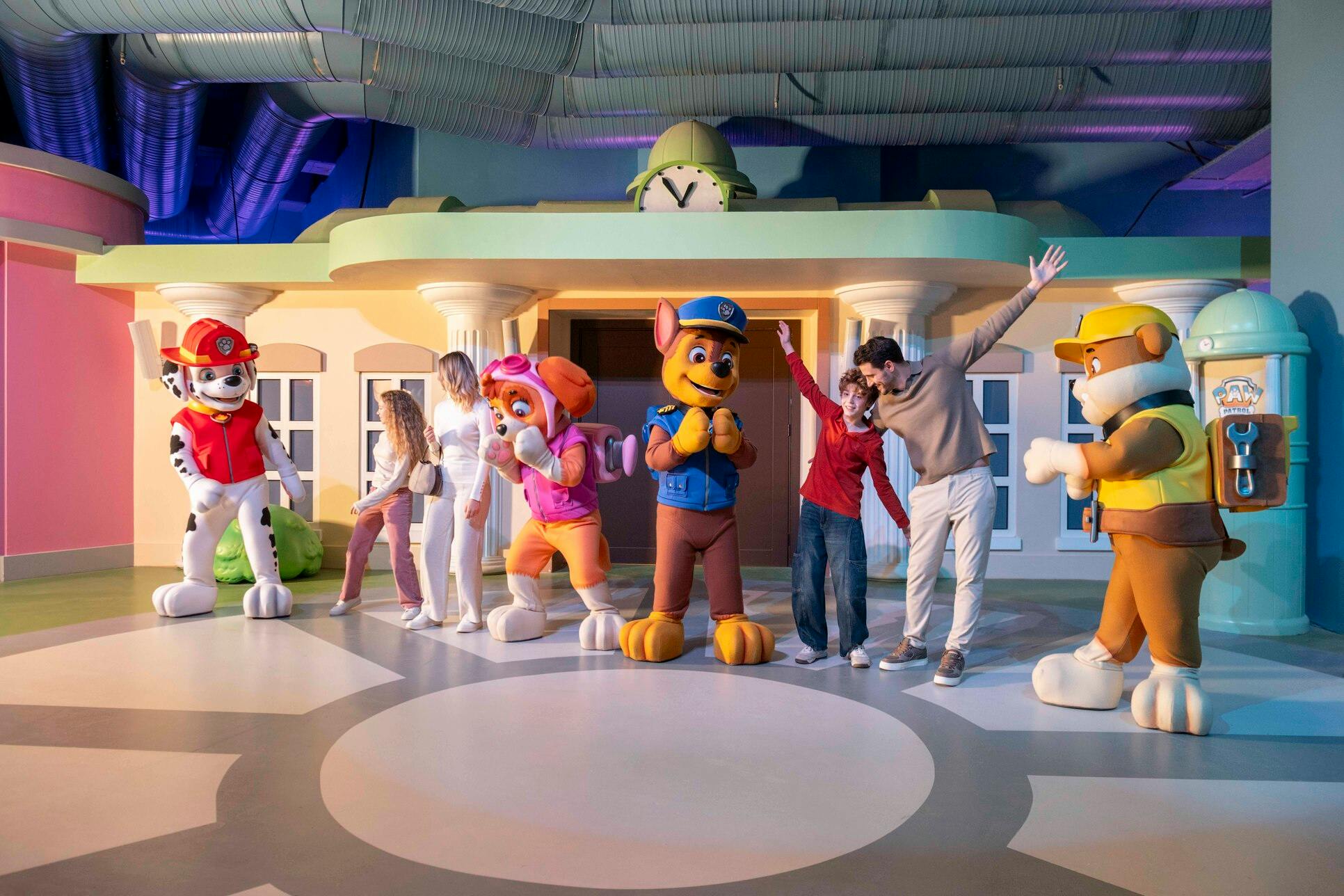 Mensen poseren met de mascottes van Paw Patrol in een kleurrijke binnenomgeving die lijkt op het hoofdkwartier van de show.