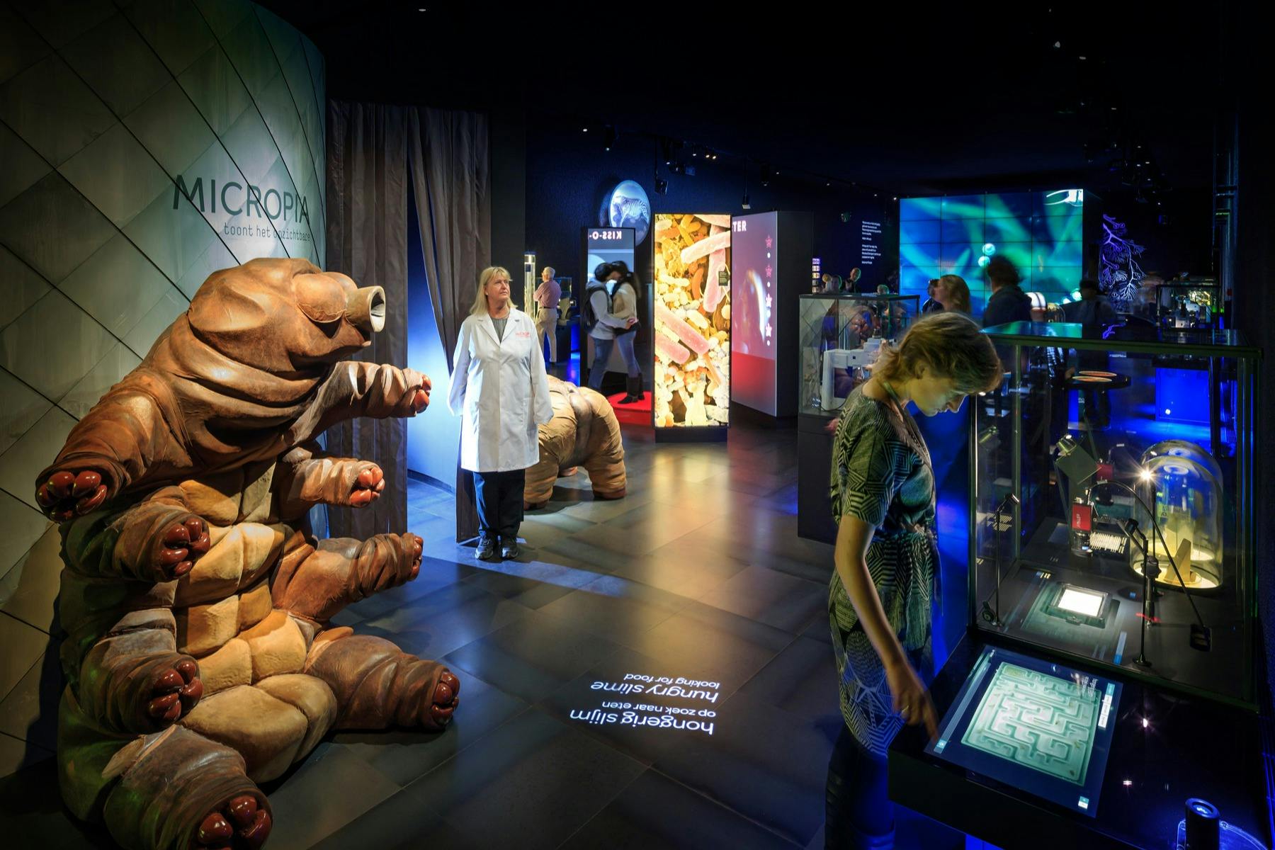 Ein Museumsexponat mit einem großen Bärtierchenmodell, einer Person in einem weißen Laborkittel und interaktiven Displays im Hintergrund.