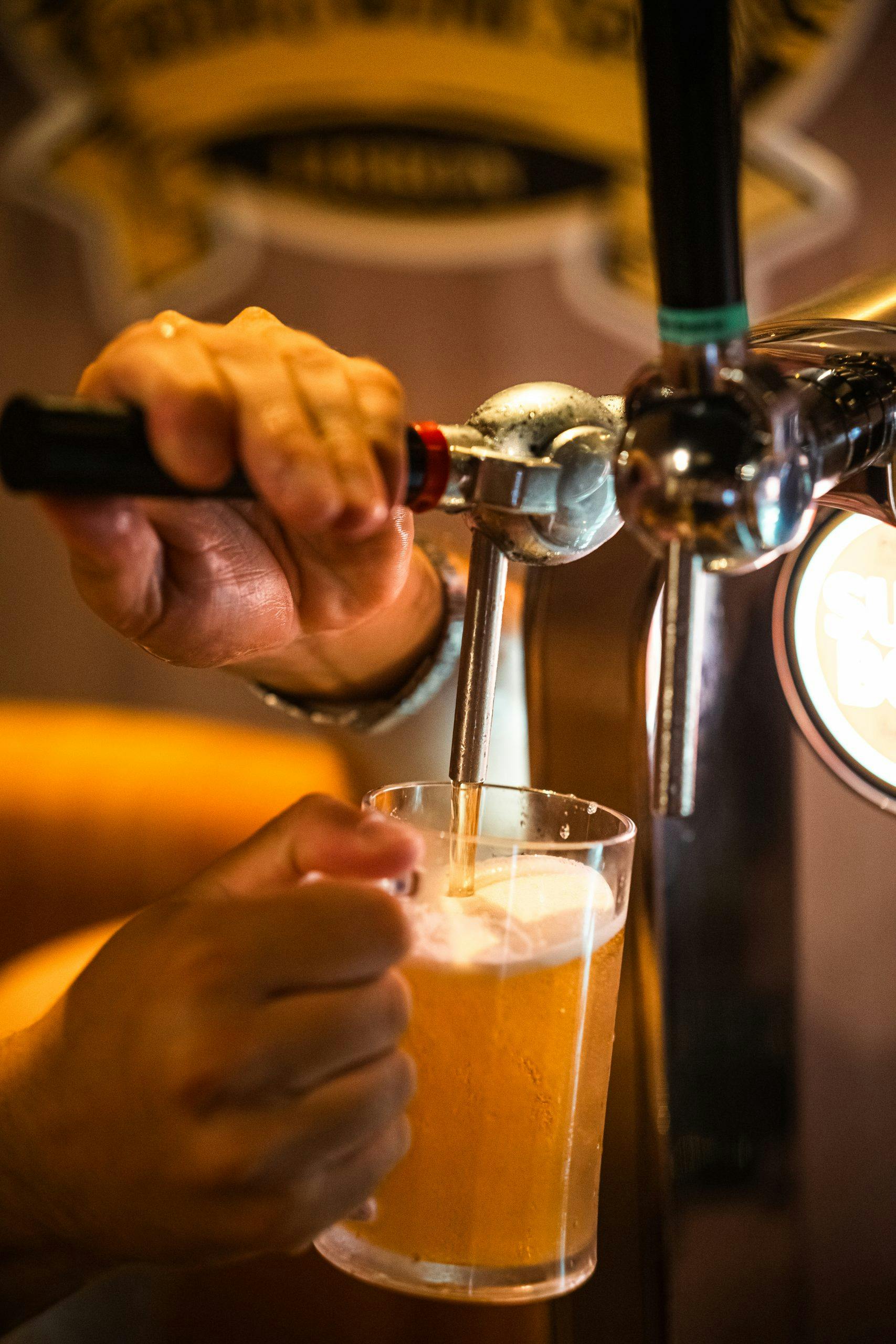 Κοντινό πλάνο ενός μπάρμαν που ρίχνει μια βαρελίσια μπύρα σε ένα ποτήρι από μια λαβή βρύσης.