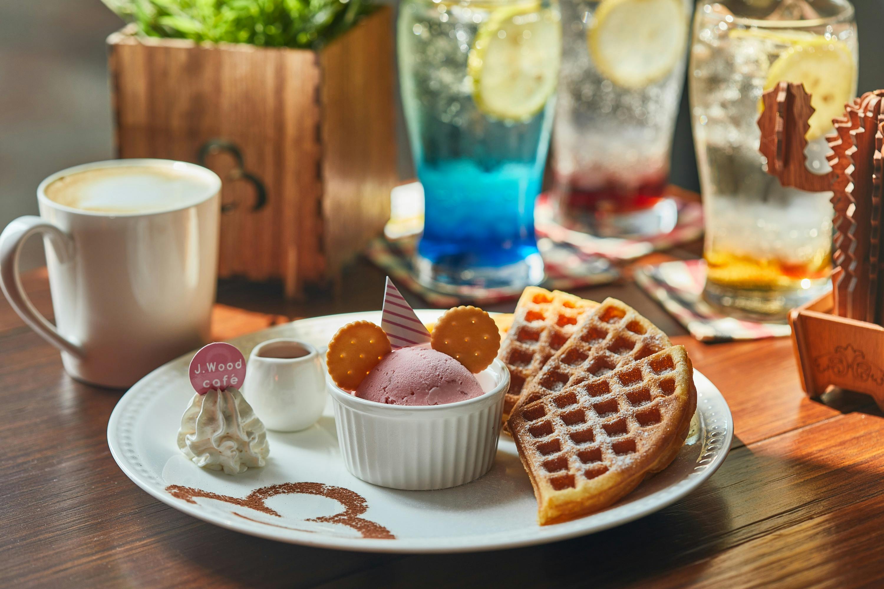 A plate with waffles, pink ice cream decorated like a face, whipped cream, a drink, and decorative elements on a table.