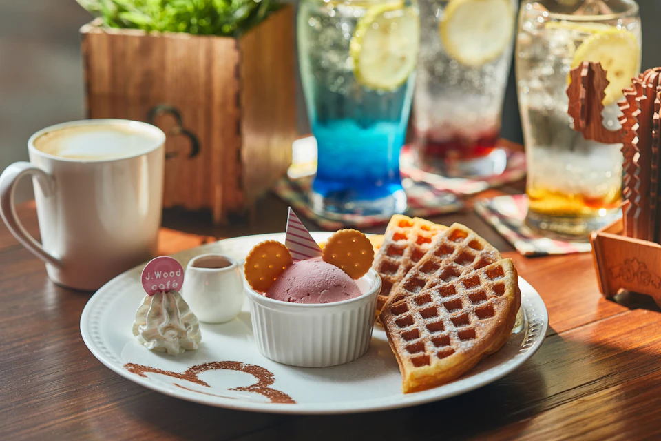 A plate with waffles, pink ice cream decorated like a face, whipped cream, a drink, and decorative elements on a table.