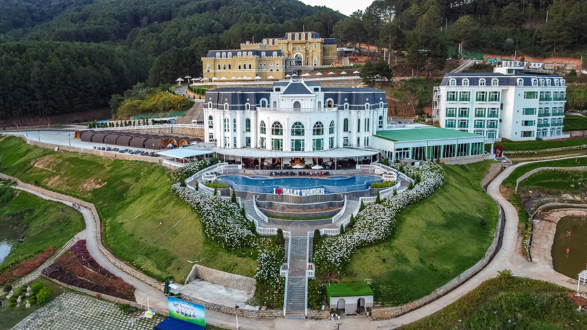 A grand white building with a garden terrace labeled "Dalat Wonder" and a staircase descending through landscaped greenery.