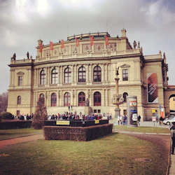 En historisk byggnad med välvda fönster, människor samlade utanför, en staty och flera skyltar, inklusive en för parkering.