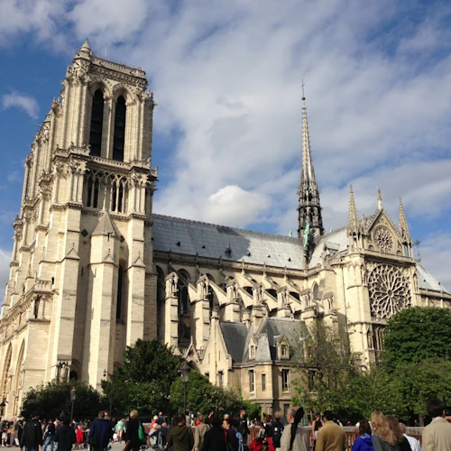Massor av människor framför Notre-Dame-katedralen i Paris, med sina torn och spiror under en delvis molnig himmel.