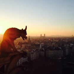 En gargoyle-staty har utsikt över en stadsbild i solnedgången, med Eiffeltornet synligt i fjärran.