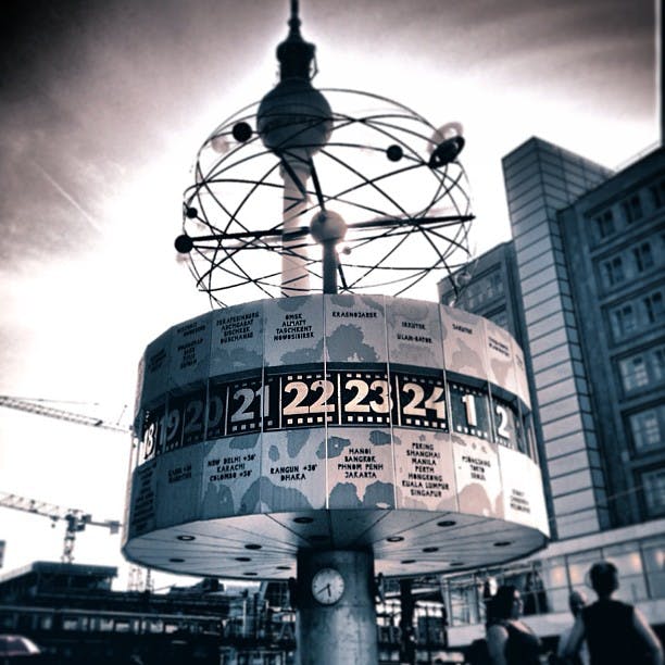 En stor världsklockstruktur med roterande indikatorer som visar flera tidszoner i en stadsbildsbakgrund.