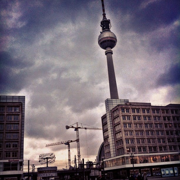 Högt TV-torn med ett sfäriskt observationsdäck, mulen himmel och omgivande byggnader med synliga byggkranar.