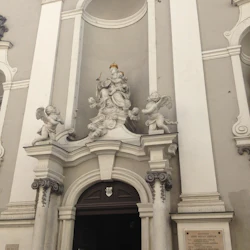 Utsmyckad kyrkoentré med statyer av änglar och en central figur ovanför dörren. En person går in i kyrkan.