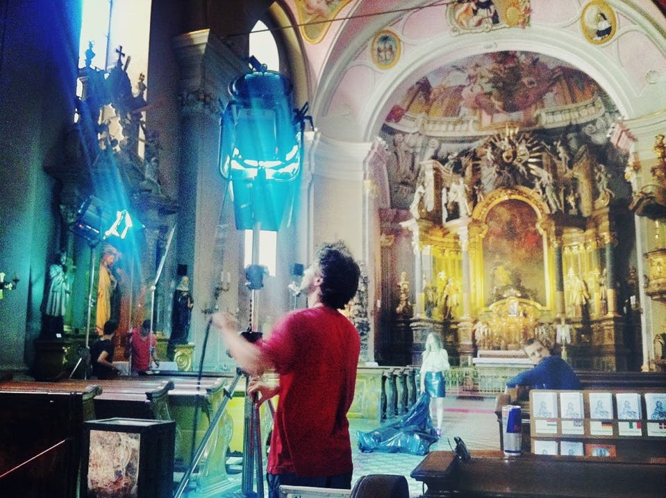 En man justerar belysningsutrustning inuti en utsmyckad kyrka, med detaljerade religiösa statyer och ett stort altare i bakgrunden.