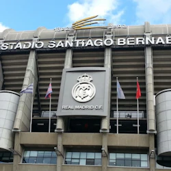 Fasaden på Estadio Santiago Bernabeu, med Real Madrid C.F. emblem, flaggor och arenans namn framträdande.