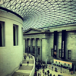 Människor som går i ett stort, atriumliknande utrymme med ett glaskupoltak i ett museum. Skyltar för "Biljetter och medlemskap" är synliga.